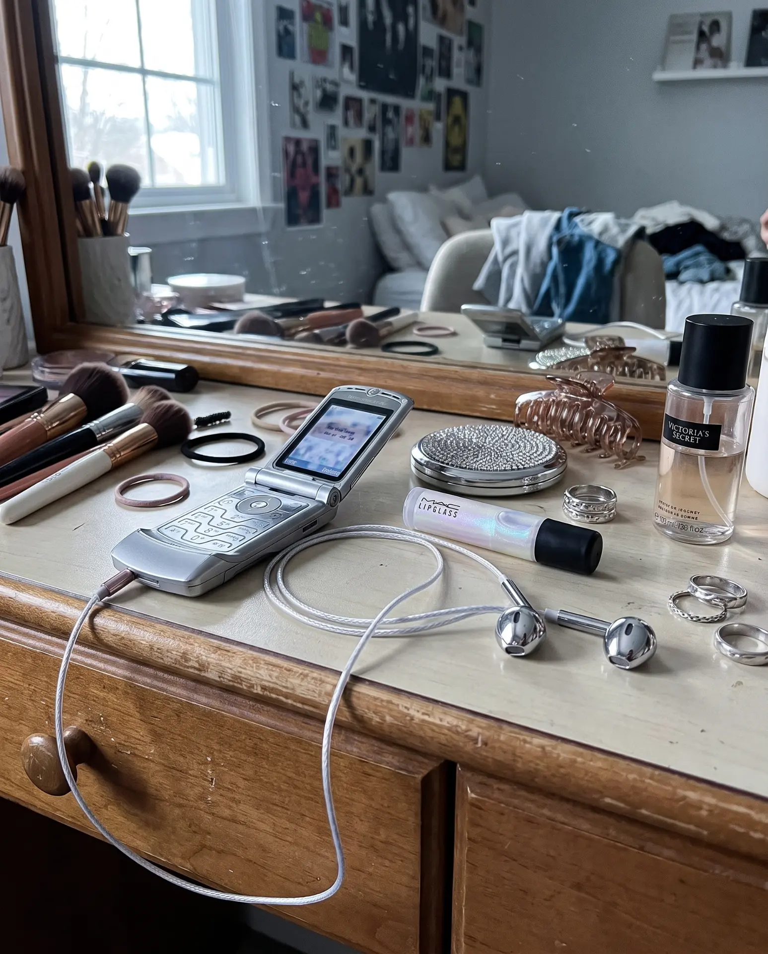 Silver Auralie earbuds on a vanity with makeup, rings and a flip phone