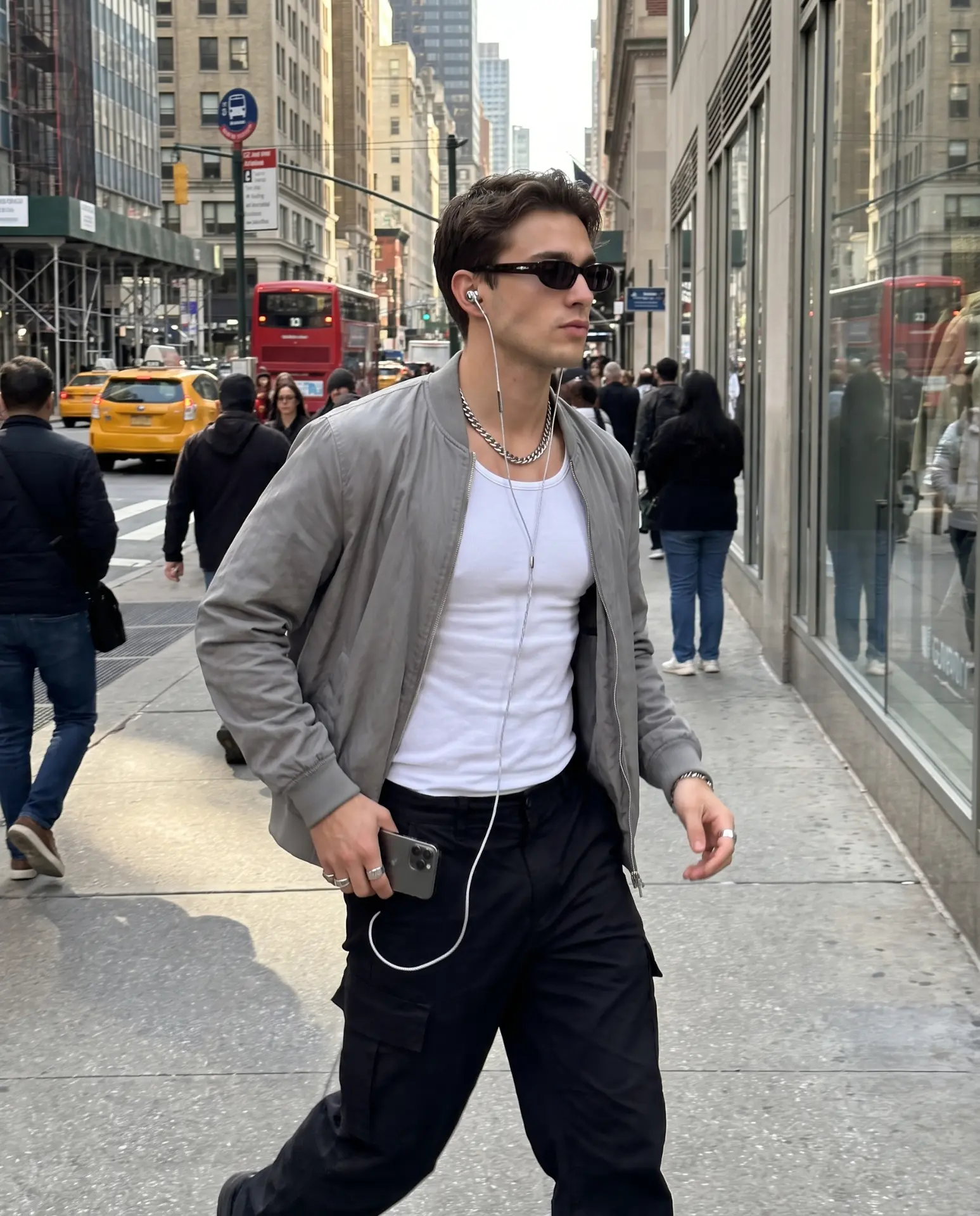 Wearing silver Auralie earbuds walking a city street in a grey bomber jacket and chain necklace