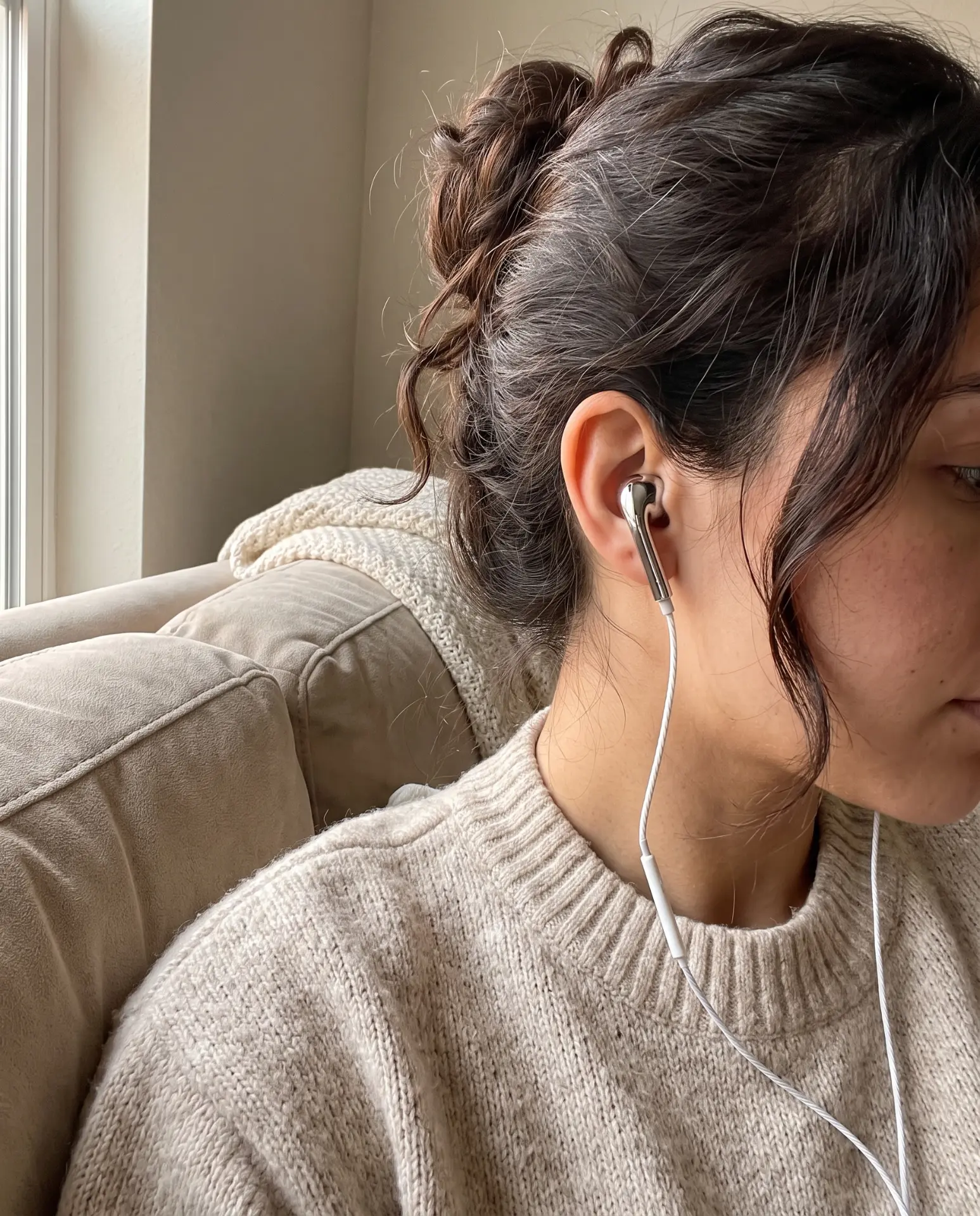Side profile wearing a silver Auralie earbud in a cosy sweater on a couch