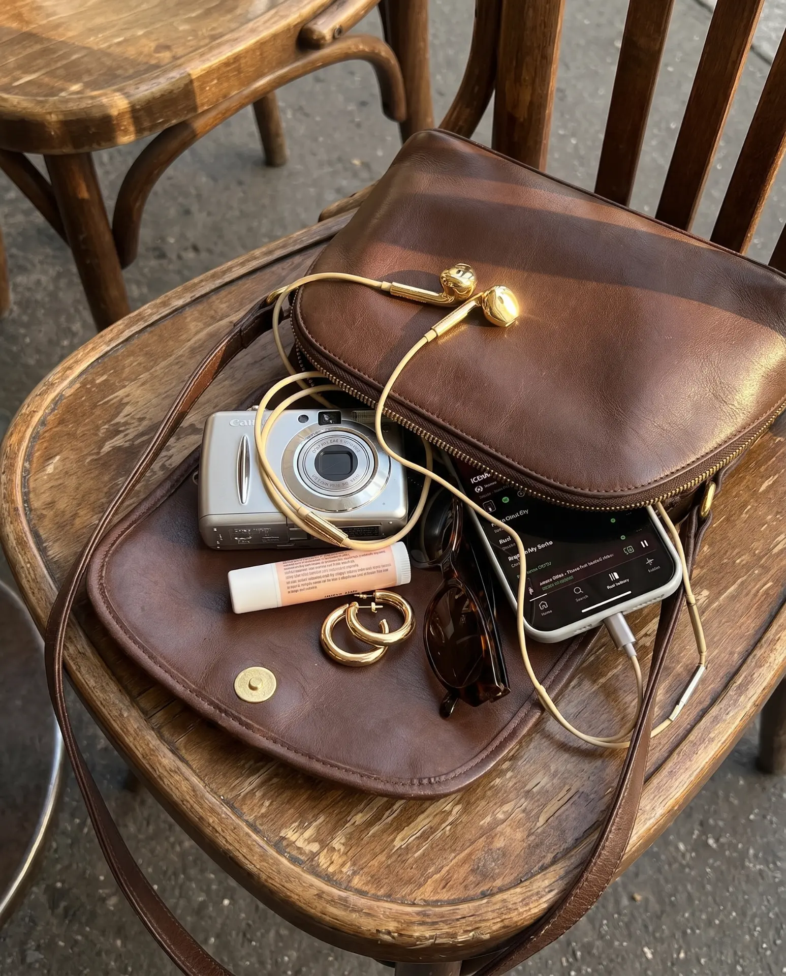 Gold Auralie earbuds resting on a leather bag at a café table
