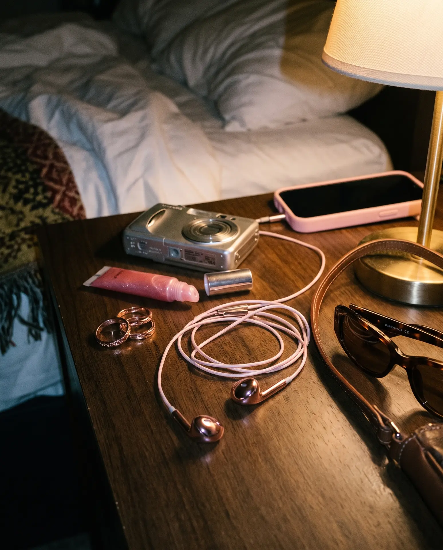 Rose gold Auralie earbuds coiled on a bedside table beside rings and sunglasses