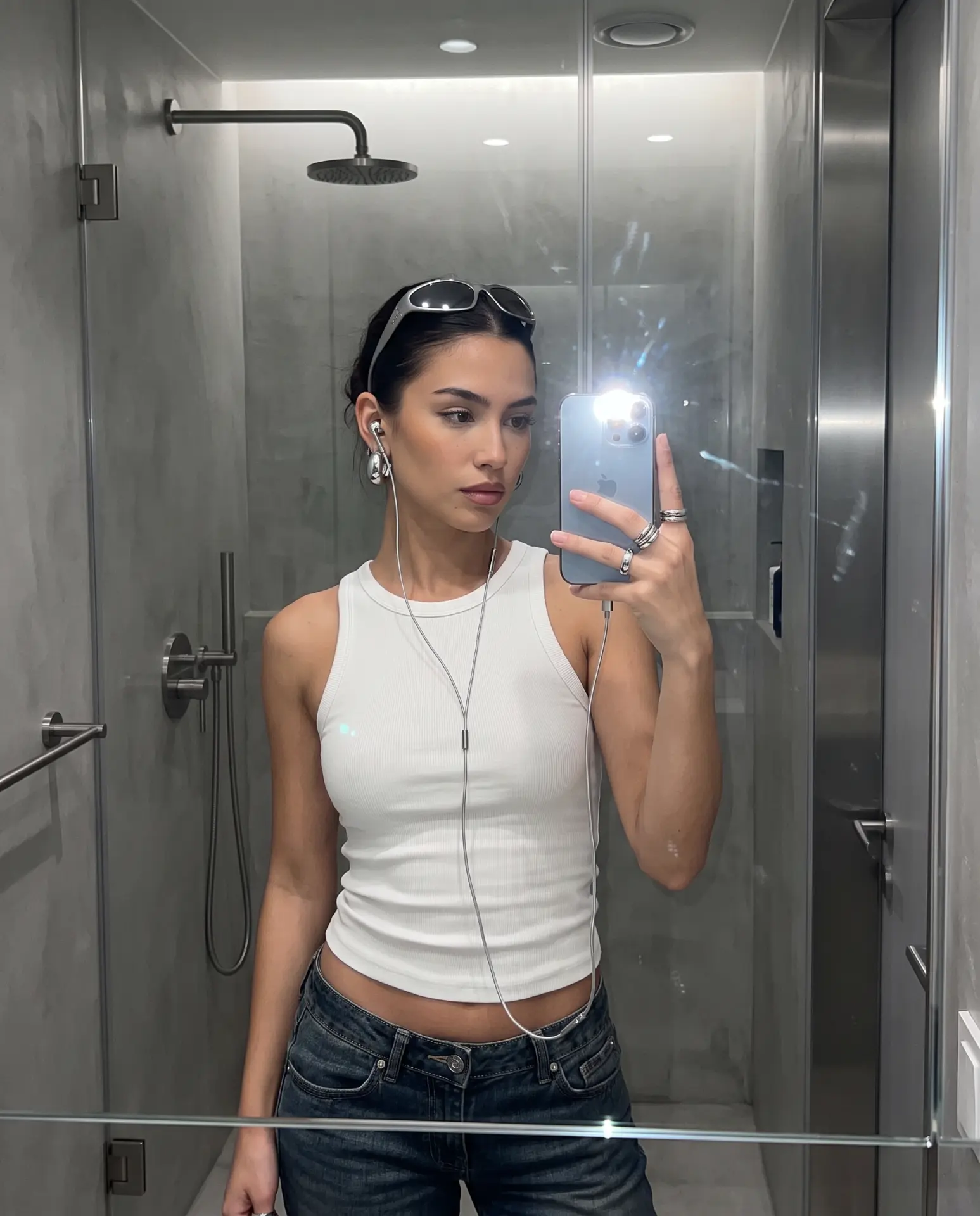 Mirror selfie wearing silver Auralie earbuds with a white tank and jeans