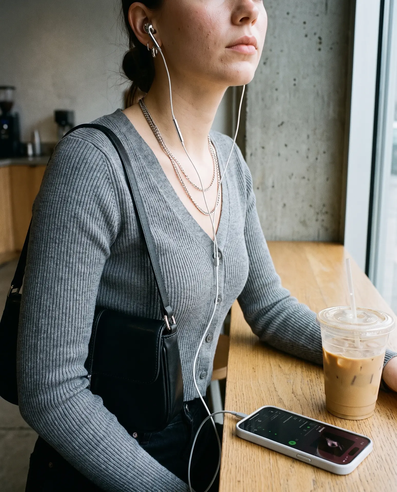 Wearing silver Auralie earbuds at a café window with layered chains